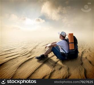 Tourist sitting in a sand desert and looking at sun