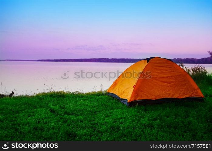 Tourist tent on the shore of a calm lake in the early morning. Pink dawn sky. Summer landscape. The concept of travel, privacy, freedom.. Tourist tent on shore of calm lake in early morning