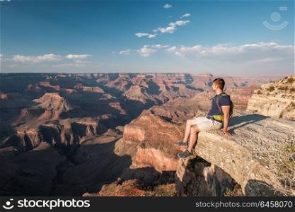 Tourist with backpack at Grand Canyon sitting on the rock edge, Arizona, USA