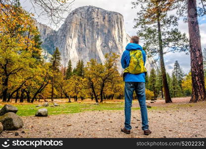 Tourist with backpack hiking in Yosemite National Park Valley at cloudy autumn morning. Low clouds lay in the valley. California, USA.