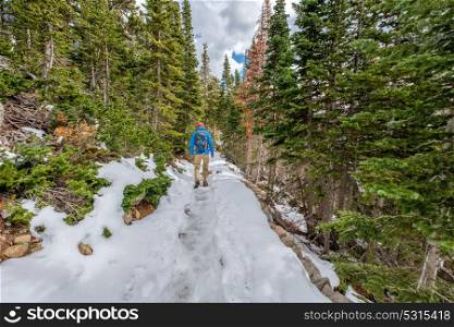 Tourist with backpack hiking on snowy trail in Rocky Mountain National Park, Colorado, USA.