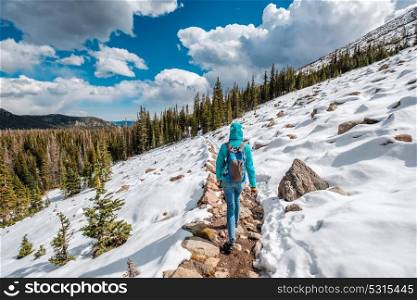 Tourist with backpack hiking on snowy trail in Rocky Mountain National Park, Colorado, USA.