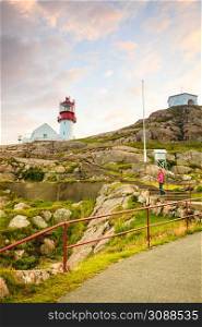 Tourist woman and historic red white lighthouse on the edge of rocky sea coast, South Norway, Lindesnes Fyr beacon. Lindesnes Lighthouse in Norway