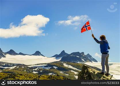 Tourist woman enjoy mountains landscape, holding norwegian flag. National tourist scenic route 55 Sognefjellet, Norway. Tourist with norwegian flag in mountains