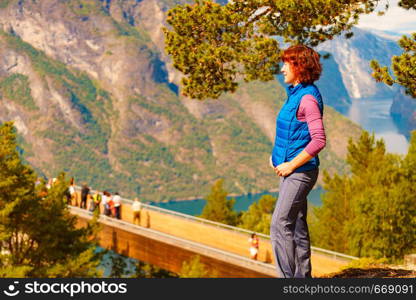 Tourist woman over Stegastein lookout looking at view of fjord mountains, Norway. Hikking, relax on trip. National tourist scenic route Aurlandsfjellet.. Tourist enjoying mountains fjord view, Norway