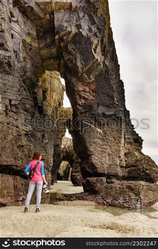 Tourist woman taking travel photo from cliff formations on Cathedral Beach in Galicia Spain. Playa de las Catedrales, As Catedrais in Ribadeo, province of Lugo, northern Spain.. Woman with camera at Cathedral Beach, Galicia Spain.