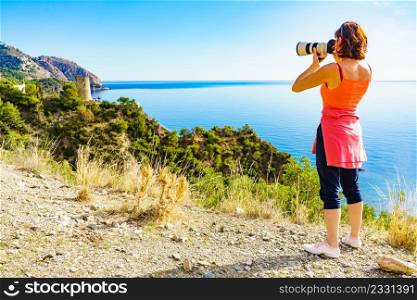 Tourist woman with camera taking travel photo from seaside cliff, mediterranean coastal landscape. Summer holiday trip.. Woman with camera take travel photo on sea shore