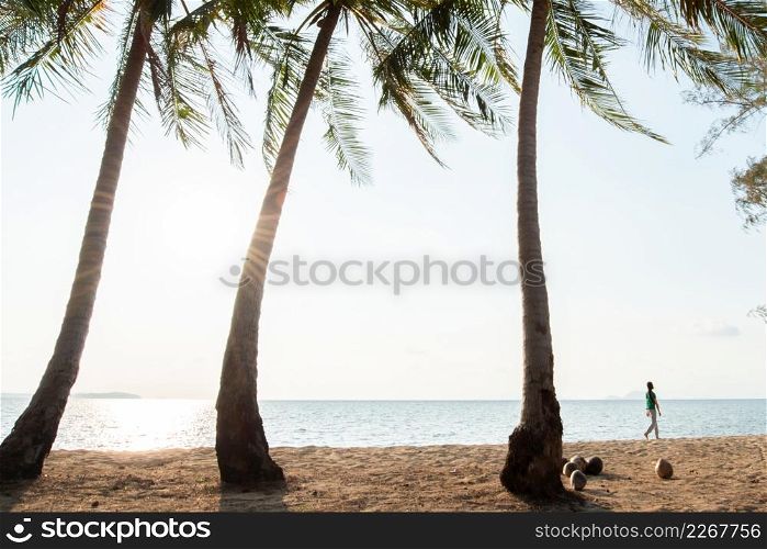 Tourist women walking on the tropical beach in the evening, coconut trees foreground, coconuts on the ground. sun setting and sea background. Summer season. Koh Mak Island, Eastern Thailand.