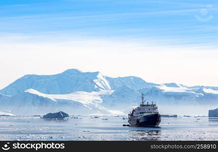 Touristic antarctic cruise liner drifting in the lagoon among the icebergs with glacier in background, Neco bay, Antarctica