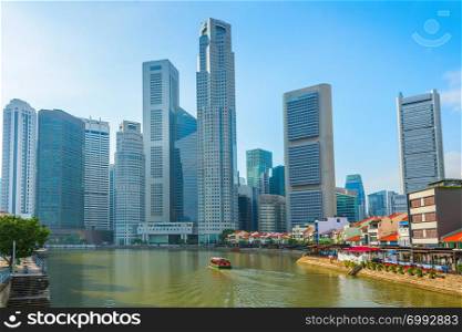Touristic boat by embankment with restaurants, modern Singapore skyline in sunshine