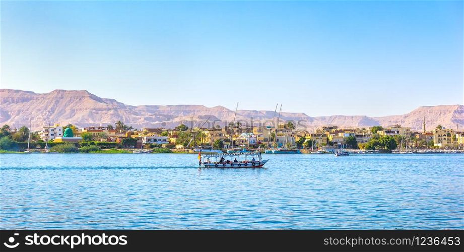 Touristic boat floating past the village on river Nile in Luxor, Egypt. Village on Nile