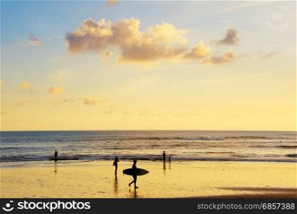 Tourists and surfers on a Bali island beach at sunset. Indonesia