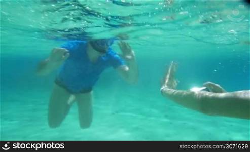 Tourists diving with smartphone. Woman taking picture or shooting video of a man in snorkel underwater. Friendly diver waving with his hand