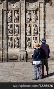 Tourists looking at ancient sculptures of Holy Door of Santiago de Compostela Cathedral. Statues from 15th century