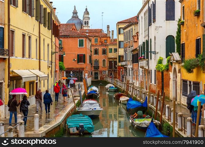 Tourists walk along a Venetian canal under umbrellas on a rainy day, Italy