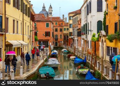 Tourists walk along a Venetian canal under umbrellas on a rainy day, Italy