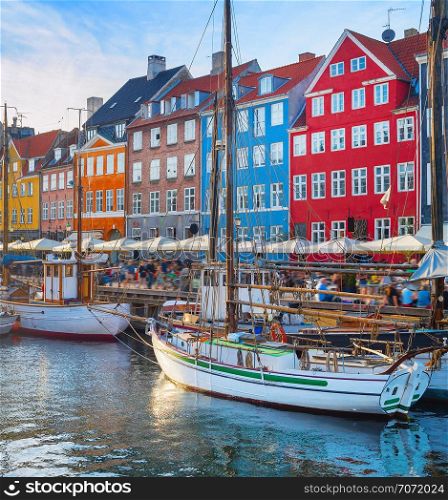 Tourists walking at Nyhavn embankment with moored tour boats at sunset, Copenhagen, Denmark