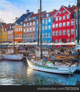 Tourists walking at Nyhavn embankment with moored tour boats at sunset, Copenhagen, Denmark