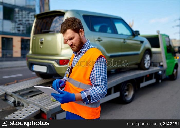 Tow truck operator checking electronic invoice document. Man with mobile tablet near evacuator. Male tow truck operator checking electronic invoice