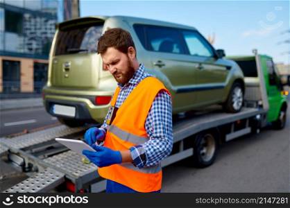 Tow truck operator checking electronic invoice document. Man with mobile tablet near evacuator. Male tow truck operator checking electronic invoice