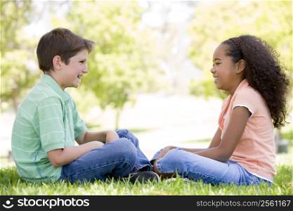Tow young friends sitting outdoors looking at each other and smiling
