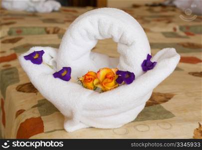Towel art: towel shaped as basket with colourful flowers inside on a hotel bed.