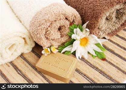 Towels and olive oil soap with aloe vera, flowers on mat background..
