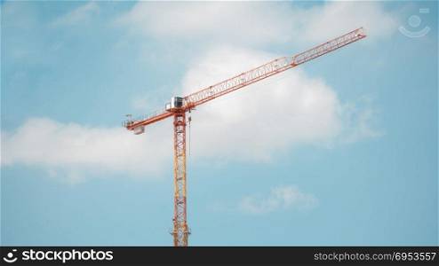 Tower crane in construction site over blue sky with clouds .
