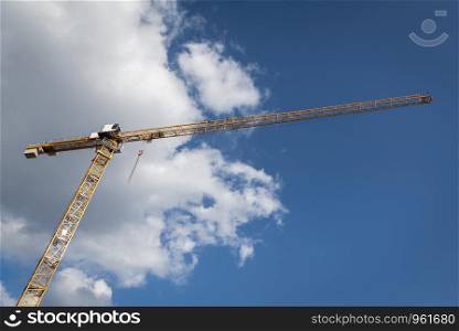 Tower crane under the blue sky. Yellow crane on construction site under a fluffy white cloud