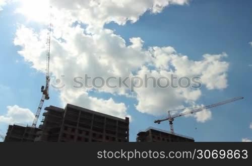 tower cranes building a house on a background of the cloudy sky