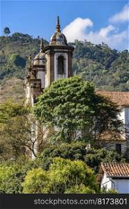 Tower of an old baroque church among the vegetation of the historic city of Ouro Preto in Minas Gerais. Tower of an old baroque church among the vegetation