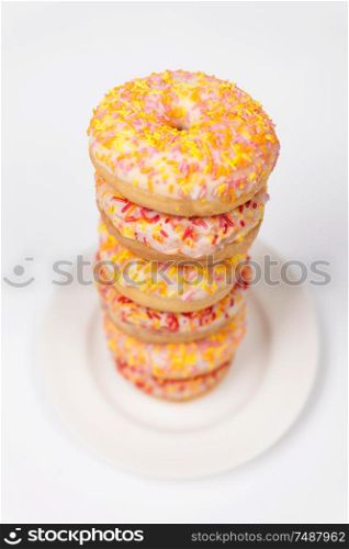 Tower of donuts or doughnuts with colorful frosting or icing and sprinkles on a white plate