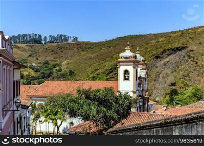 Tower of historic baroque church among the houses, roofs and hill in the city of Ouro Preto in Minas Gerais. Tower of historic baroque church