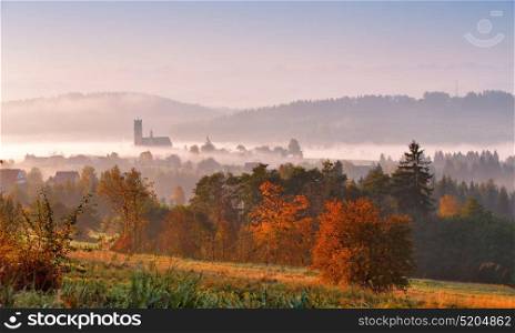 Tower of rural church in misty autumn morning. Autumn colorful morning with fog and sun rising over a mountain village. Sunrise Poland scene