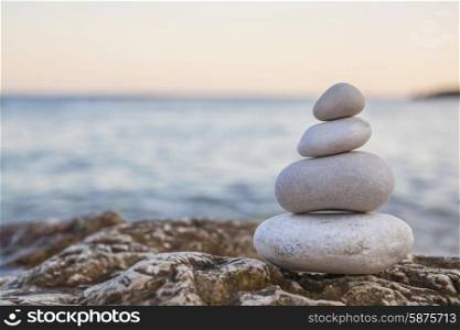 Tower of stones piles on top of a rock on a tranquil deserted beach at evening sunset
