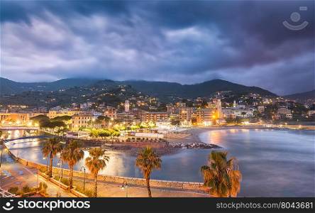 Town &amp; beach of Ventimiglia in northern Italy lit up at night under dark moody skies