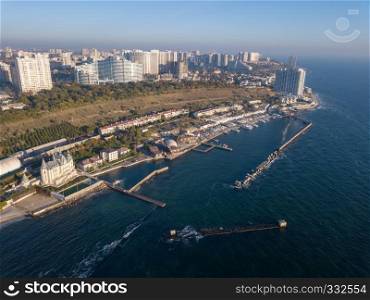 Town coastline with modern buidings, waterfront and sea beach with blue water on a background of blue sky. Aerial view from drone.. Natural landscape with costline of city Odesa, Ukraine. Seascape with sandy beach and blue water. Aerial view from drone.