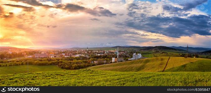 Town in green fields of mountain valley. Beautiful spring sunset above the city on a hills. Panorama
