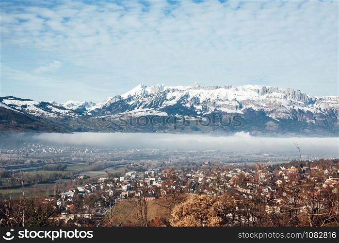 Town of Vaduz the capital of Liechtenstein, fog above the river and snow mountains of Switzerland overlooking from hilltop