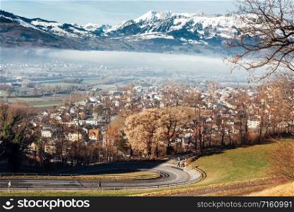Town of Vaduz the capital of Liechtenstein, fog above the river and snow mountains of Switzerland overlooking from hilltop