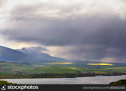 Town on the lake behind the foothills. Spring rain and storm in mountains. Green spring hills of Slovakia. Spring stormy scene.