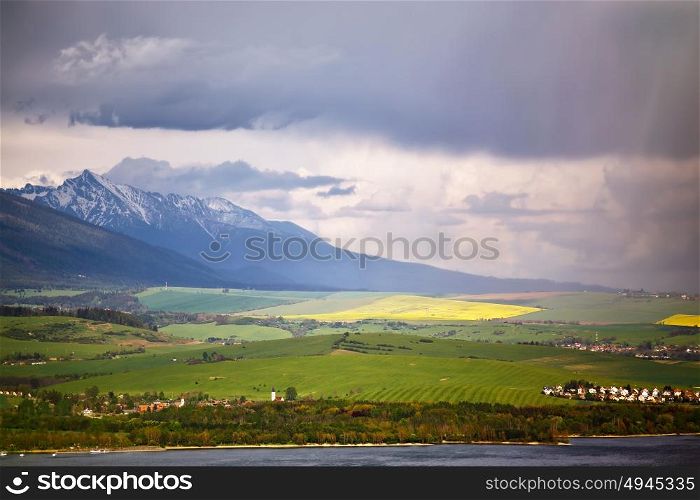 Town on the lake behind the foothills. Spring rain and storm in mountains. Green spring hills of Slovakia. Spring stormy scene.