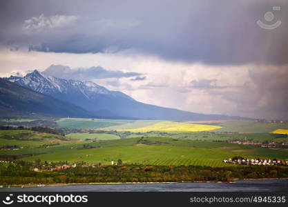 Town on the lake behind the foothills. Spring rain and storm in mountains. Green spring hills of Slovakia. Spring stormy scene.