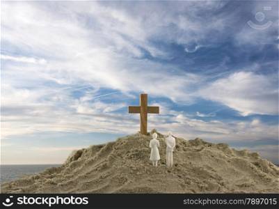 toy couple looking at the wooden holy cross on sand mountain