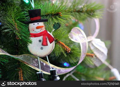 Toy funny iron snowman hanging on Christmas tree. New Year, holiday background with place for text. Pine decorated with ribbons and garlands. Front view. Horizontal.