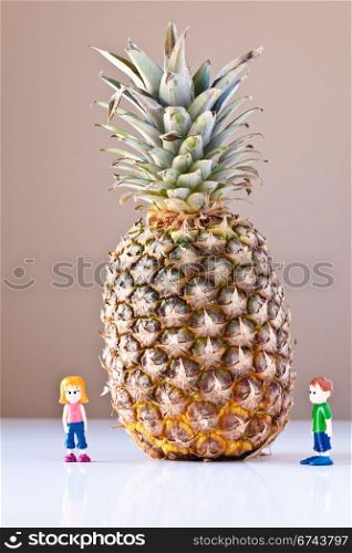 Toy girl and boy are overwhelmed by nutrition and healthy choices next to a giant pineapple. The concepts depicted in this image are nutrition, good food choices, balanced diet and good for you.