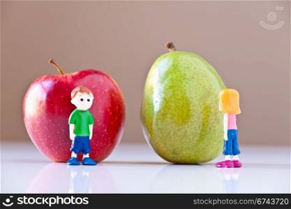 Toy girl and boy disagree over nutrition and healthy choices in front of a green pear and a red apple. The concepts depicted in this image are nutrition, good food choices, balanced diet and good for you.