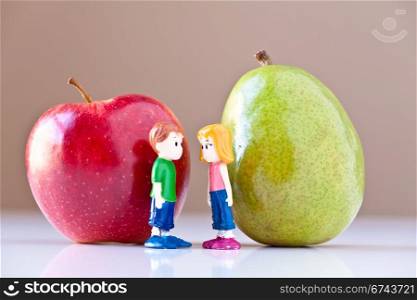 Toy girl and boy discuss nutrition and healthy choices in front of a green pear and a red apple. The concepts depicted in this image are nutrition, good food choices, balanced diet and good for you.