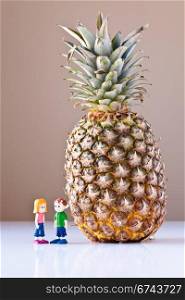 Toy girl and boy discuss nutrition and healthy choices next to a giant pineapple. The concepts depicted in this image are nutrition, good food choices, balanced diet and good for you.