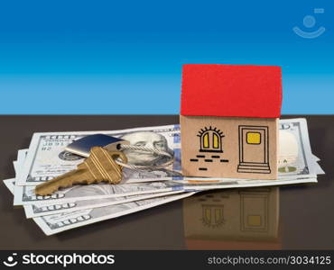 Toy house on US dollar bills with door key. Toy wooden home on US 100 dollar bills with a door key and lock to illustrate house purchase or rental. Mortgage payments to a bank are implied.. Toy house on US dollar bills with door key